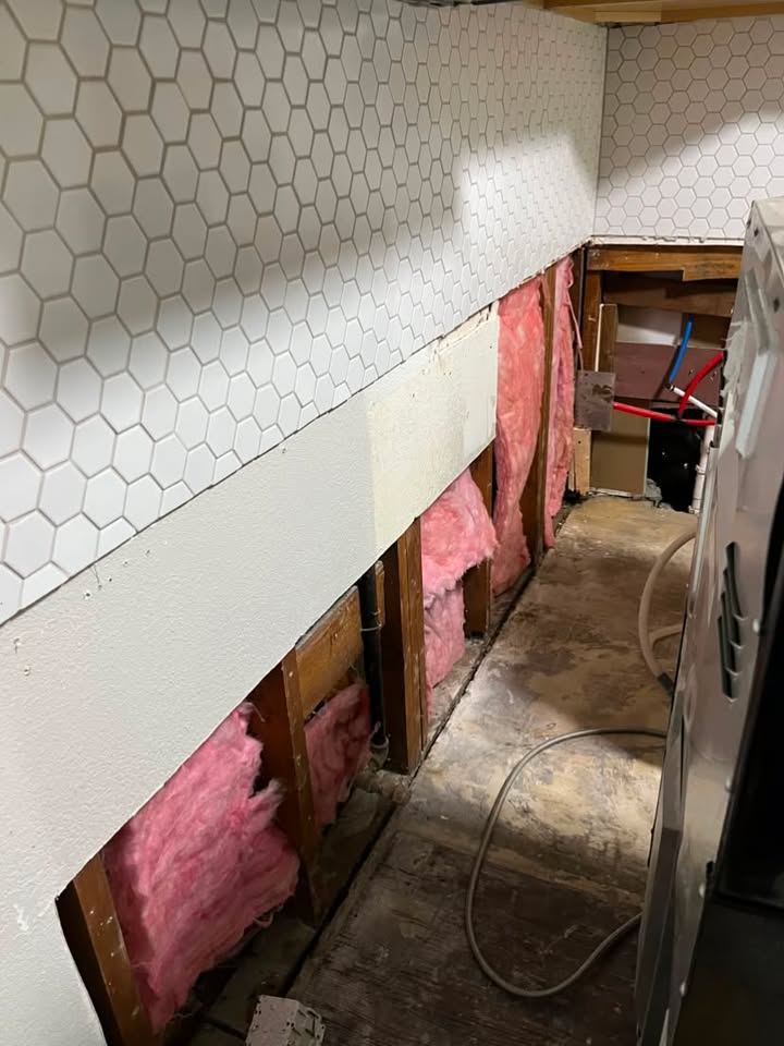 Kitchen wall opened below the hex tile backsplash, studs and insulation exposed