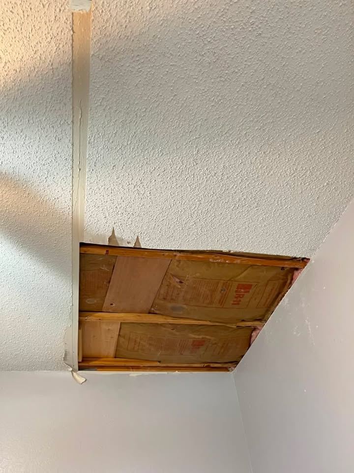 Rectangular access cut in a popcorn ceiling exposing insulation above