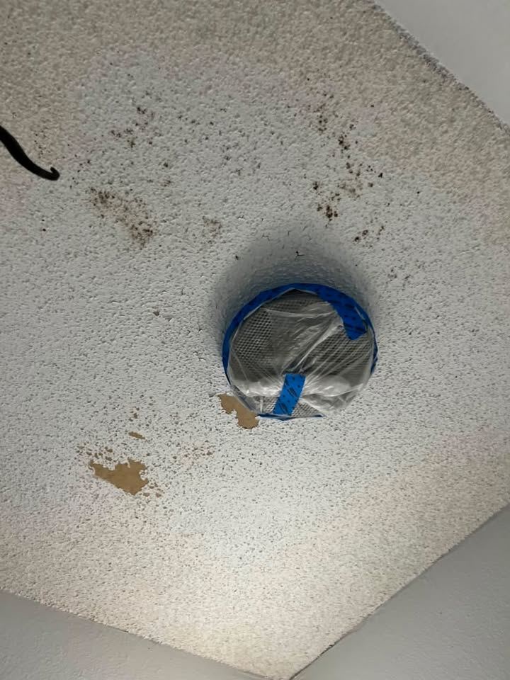 Stained, speckled popcorn ceiling with the light fixture taped off