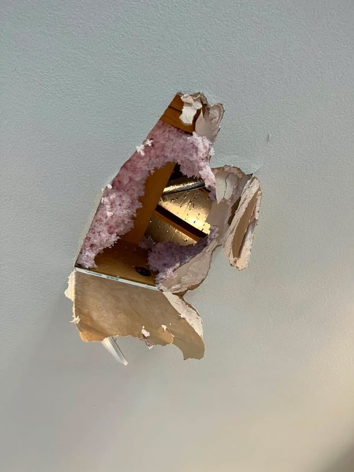 Hole broken through drywall exposing pink insulation and framing inside the wall